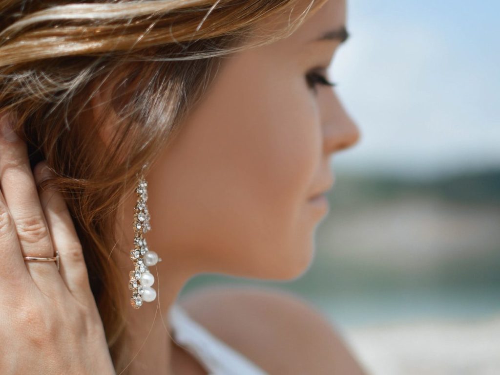 shallow focus photography of woman wearing dangling earrings holding her hair near mountain
