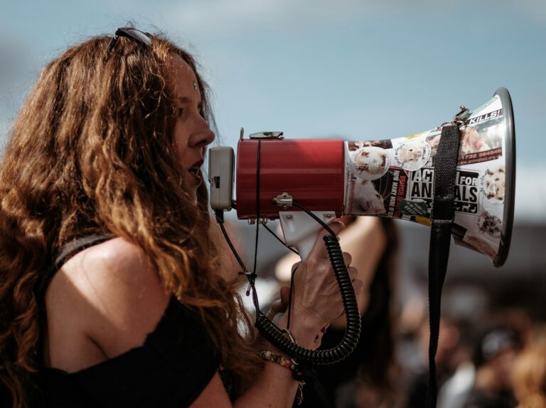 selective focus photography of woman wearing black cold-shoulder shirt using megaphone during daytime