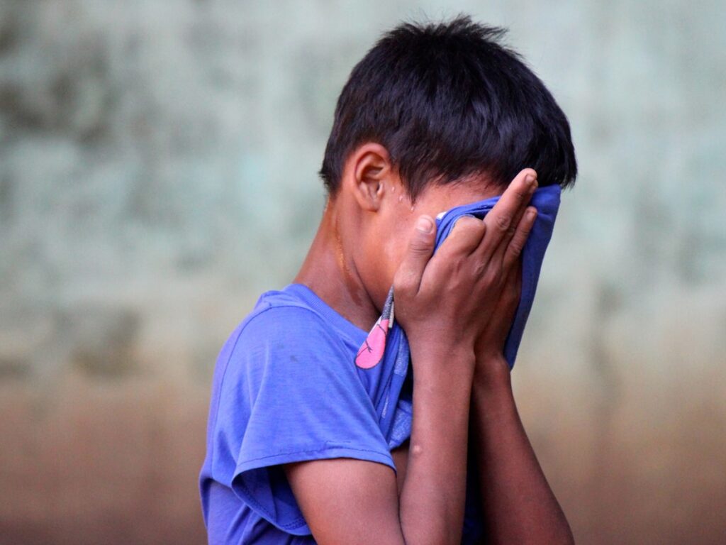 boy in blue shirt covering his face